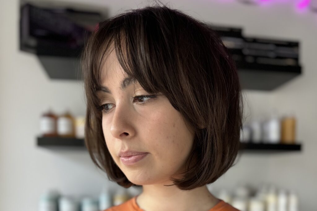 A brown-haired woman with the soft, layered bob with curtain bangs hairstyle looks pensively into the distance.