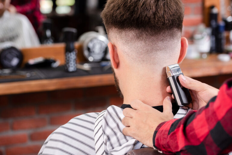 Barber using clippers to shape the neckline of a man's fresh skin fade haircut in a barbershop with brick and mirror background.
