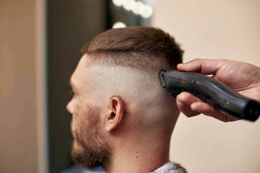 Barber using electric clippers to create a skin fade on the side of a man's head during a haircut session.
